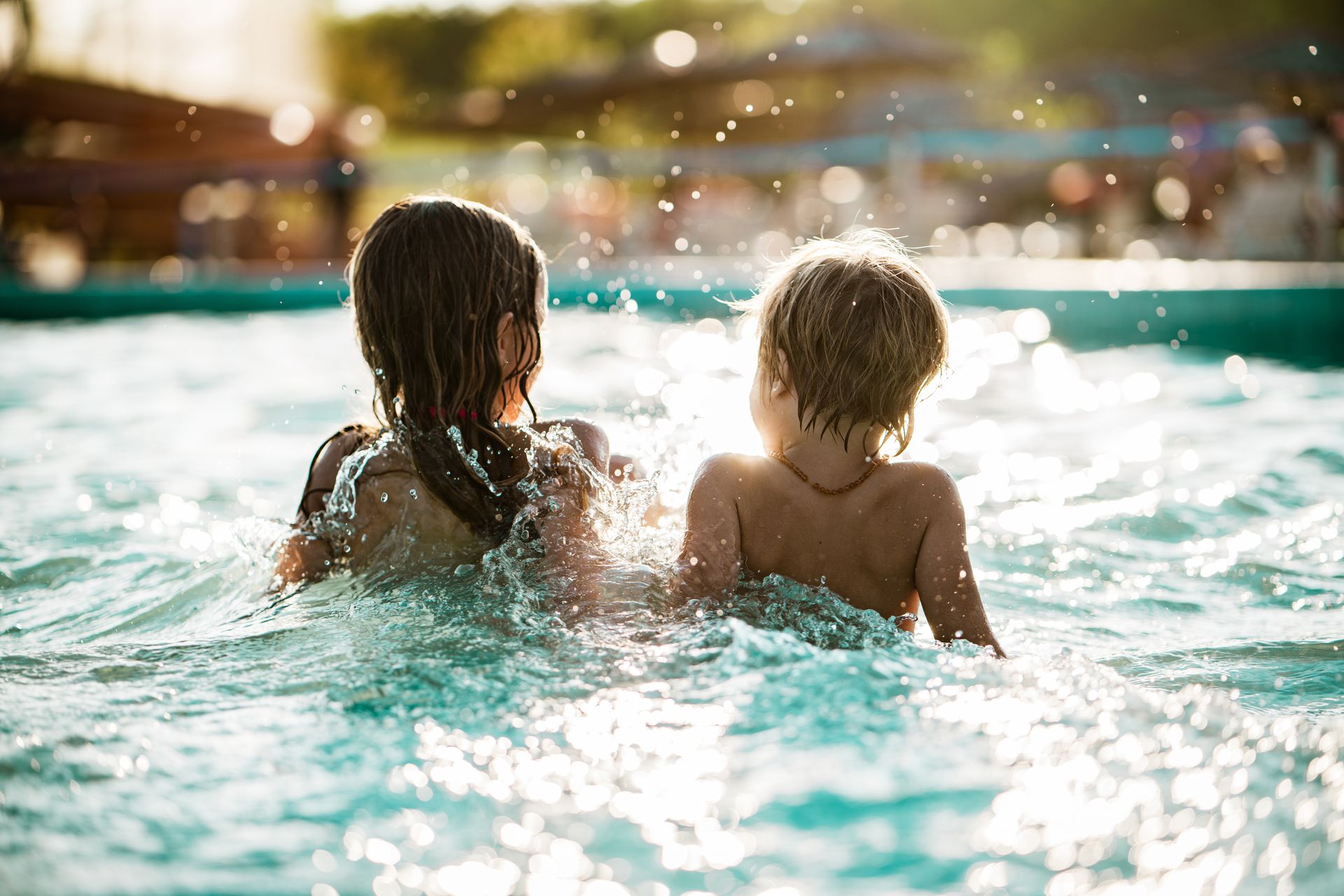 Children playing and splashing in a sunlit outdoor resort-style pool