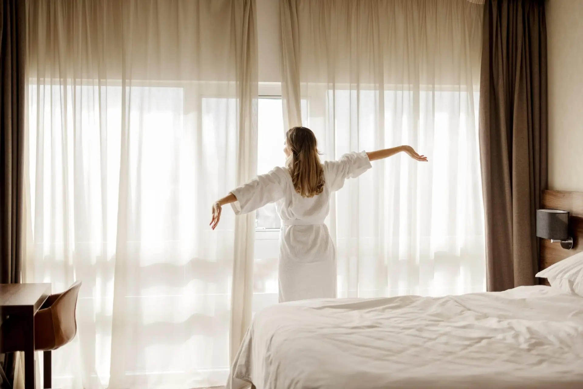 Woman stretching contentedly in a bright, elegantly furnished bedroom at Lakeridge at Hamlin